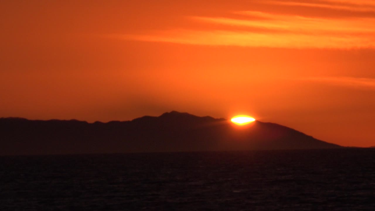 At 0:01 in Huntington Beach, California, the sun remains bright near the ridge edge above a dark ocean band, with no visible people.