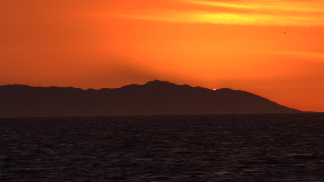 Silhouetted hills and dark sea beneath a bright orange sky.
