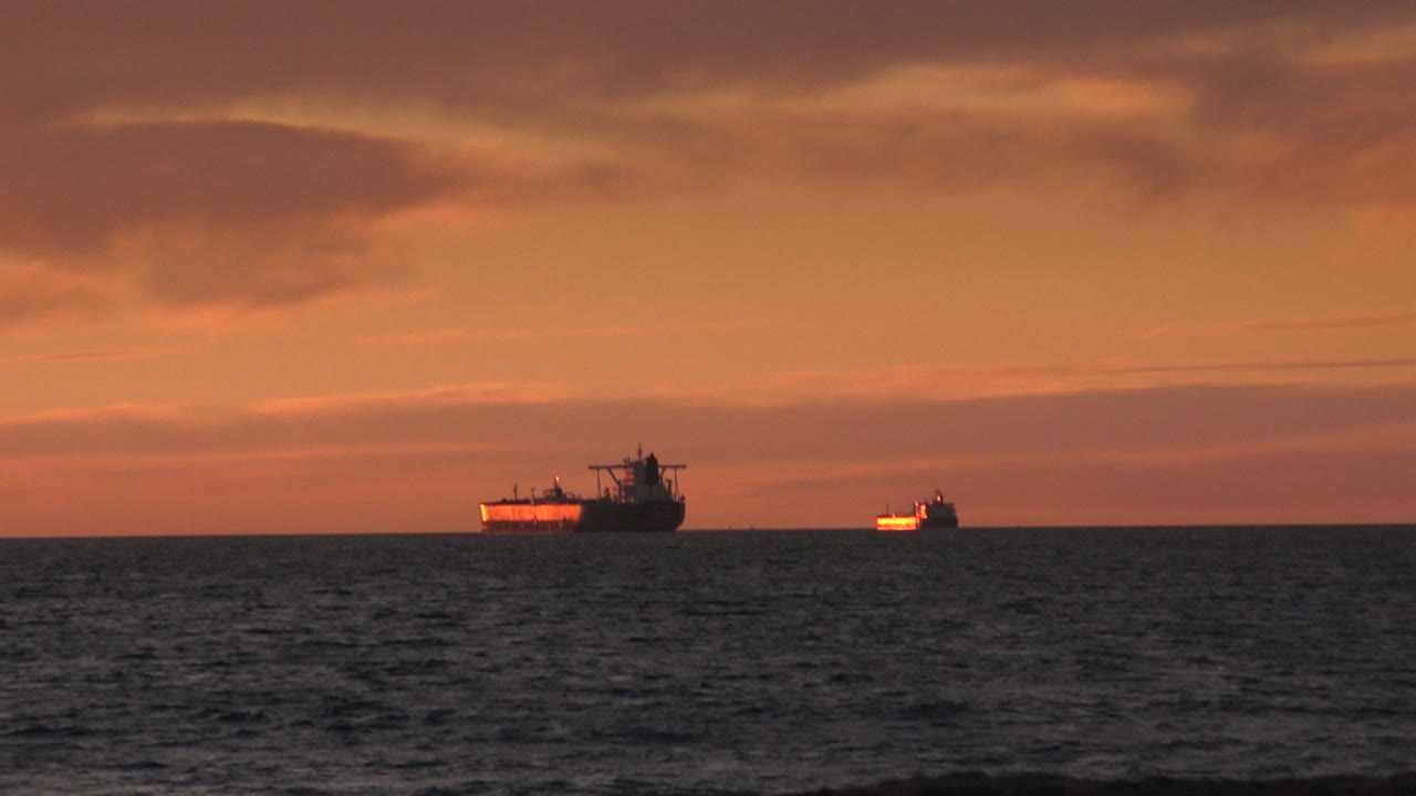Two distant vessels on a dark sea under layered sunset clouds.
