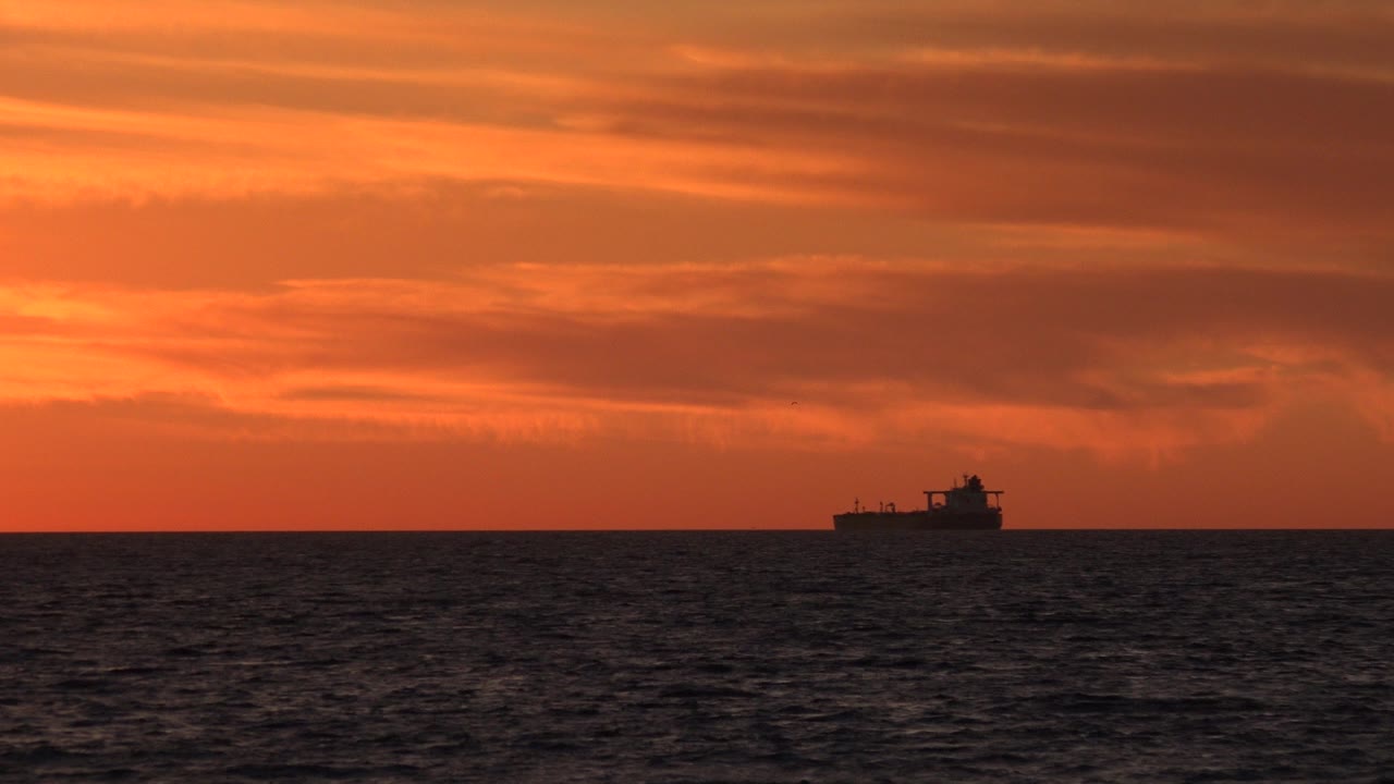 At 0:00 in Huntington Beach, California, a small dark boat sits near the horizon beneath layered orange sunset clouds, with no visible people.
