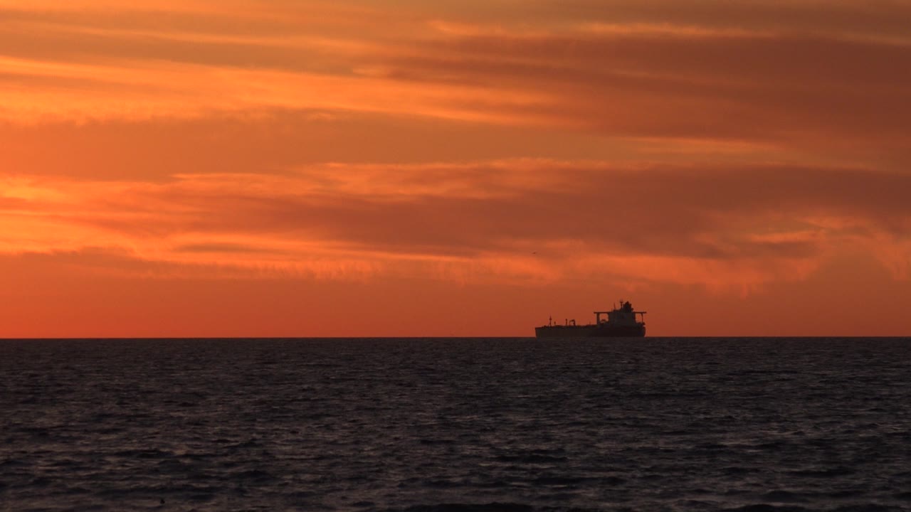 Small boat silhouette against a glowing orange cloud bank over the ocean.