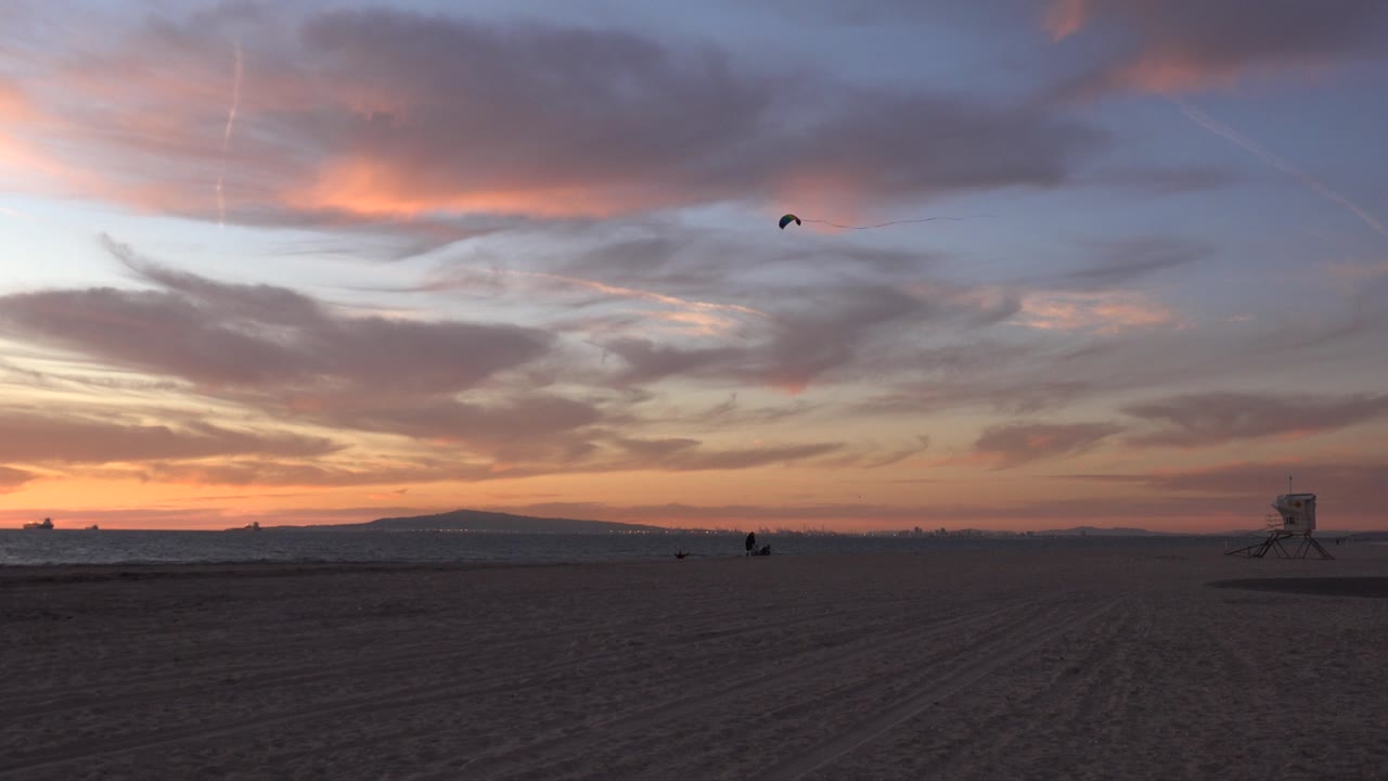 Wide sunset beach with a small kite above the horizon.