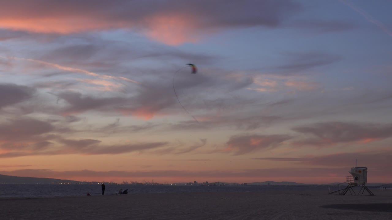 Sunset beach with kite, distant people, waves, and lifeguard tower.