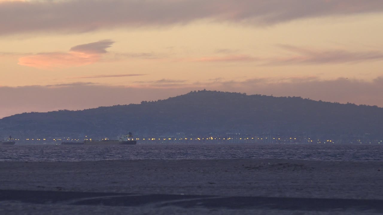 Ocean and distant hills under a peach-gray sunset sky.