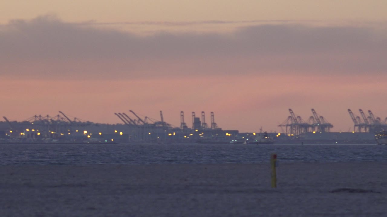 Low coastal horizon with port cranes beneath layered sunset clouds.