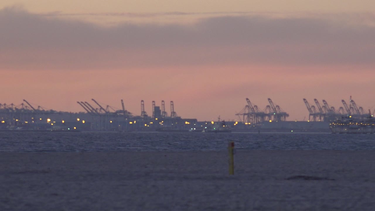 Yellow beach marker in front of distant industrial cranes at dusk.