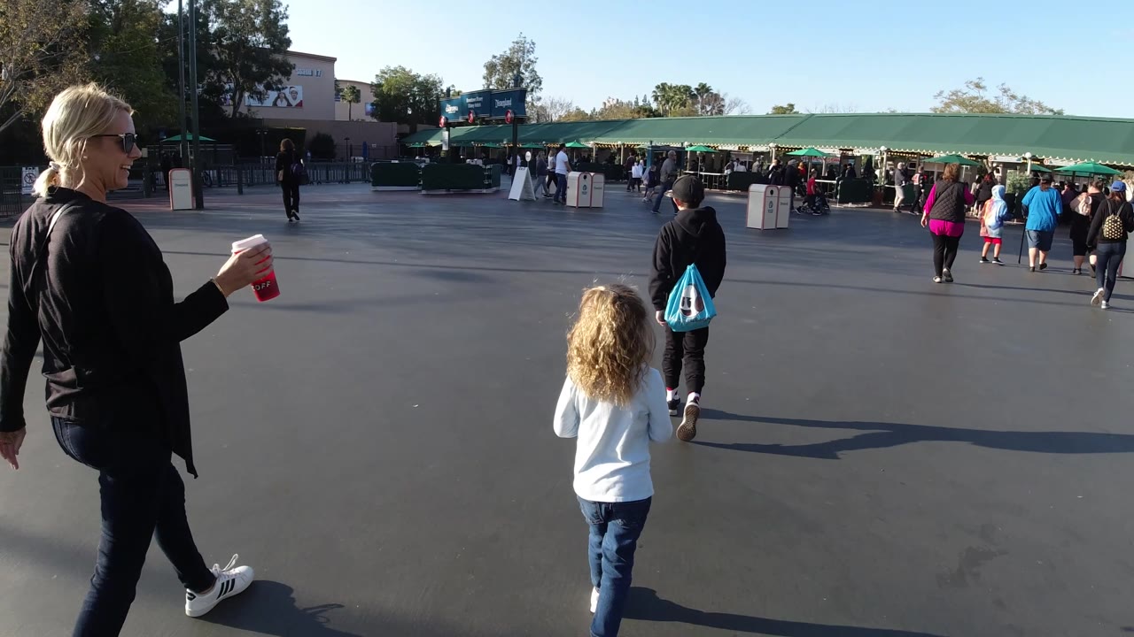 Woman and child walking across open pavement toward a busy gate area.