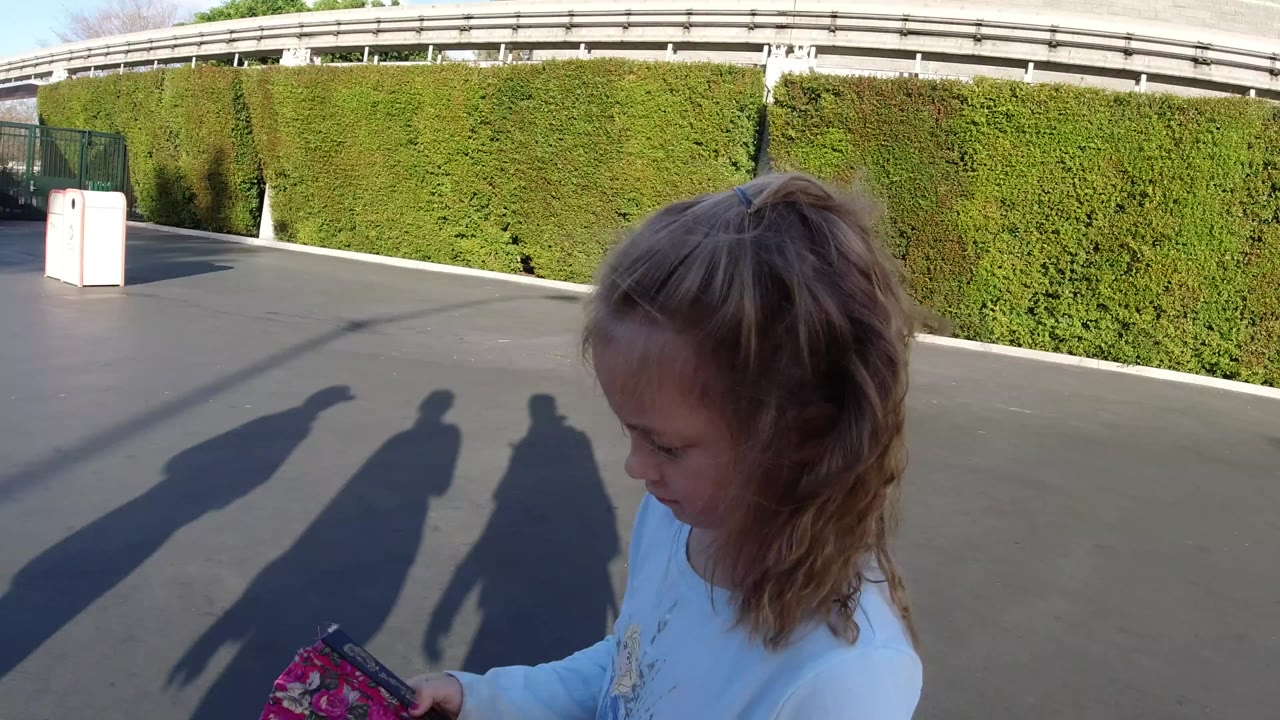 Young girl looking down at a folded fan on sunny pavement.
