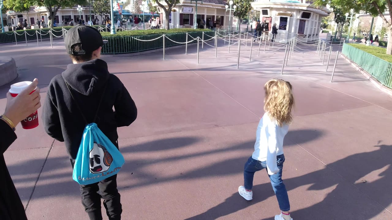 Children walk beside rope queue rails as an adult hand holds a red cup.
