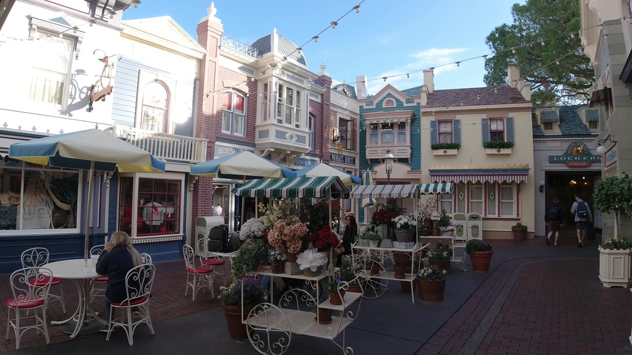 Outdoor dining chairs and flowers in front of decorative building facades.