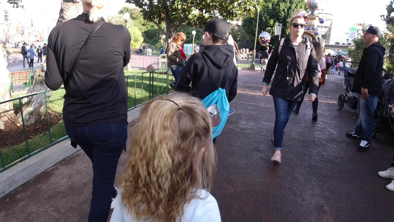 Woman in black walking ahead on a park path with visitors nearby.