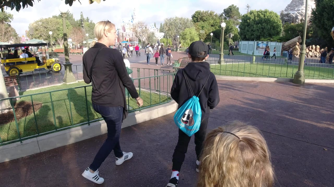 Adult and child walk past railings with a yellow vehicle at left.