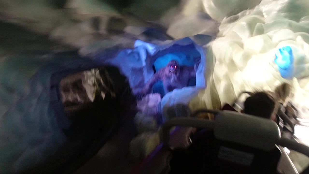 Coaster view through a tunnel toward blue lighting and riders ahead.