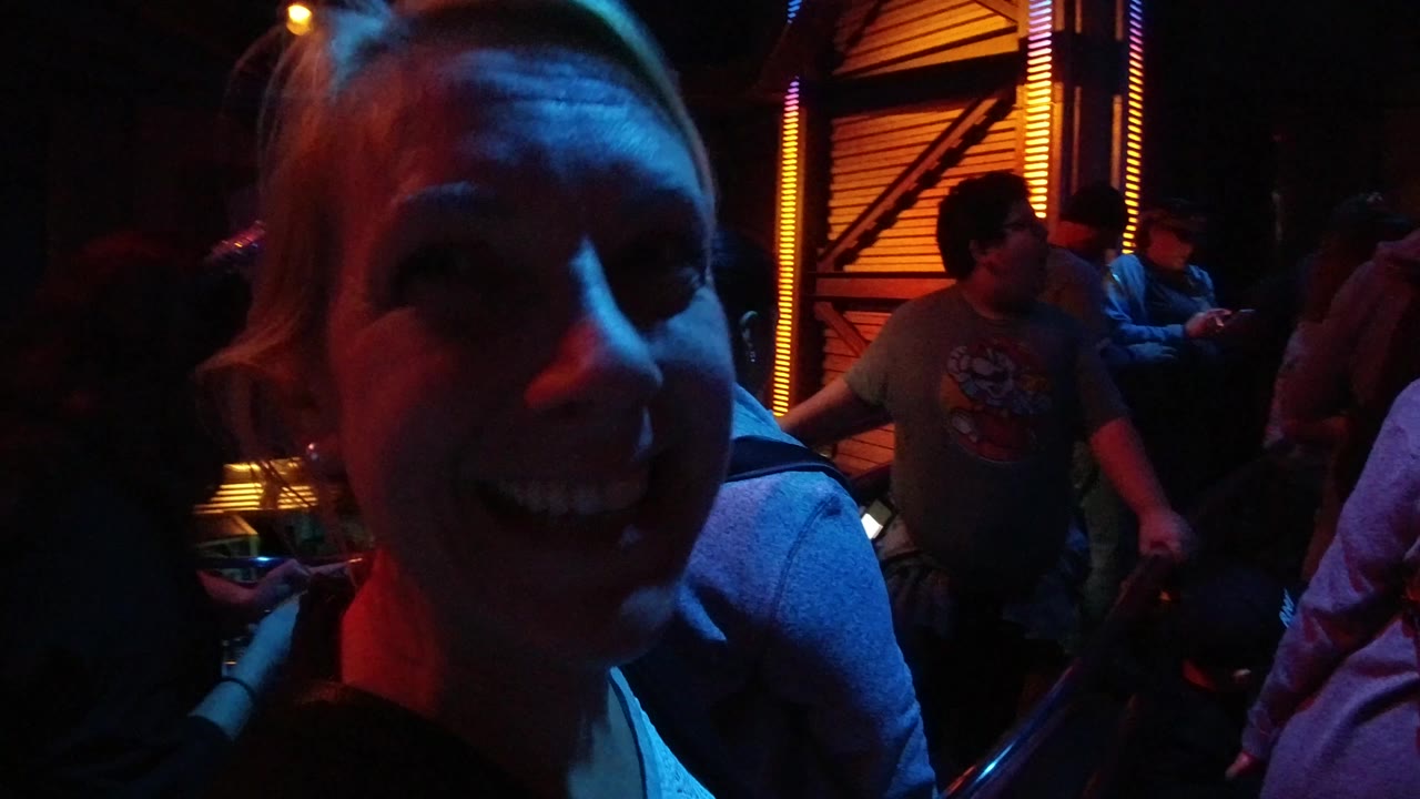 A smiling woman fills the left foreground at Disneyland California while other guests stand behind her in red and blue indoor lighting.