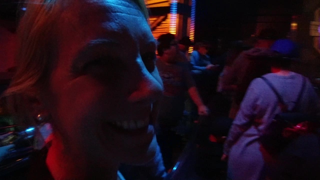 A close side view of the woman appears at Disneyland California while people pass through the dark themed interior under saturated red and blue light.