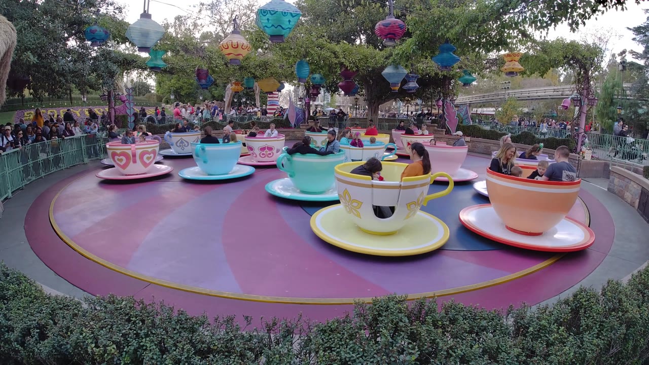 Multiple cup-shaped ride cars with families and children on an amusement park platform.