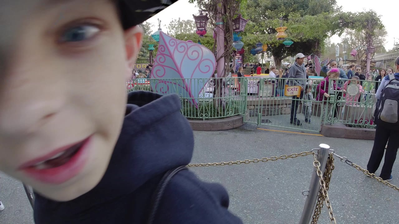 Close side view of a boy near a fenced ride entrance with crowds in the background.