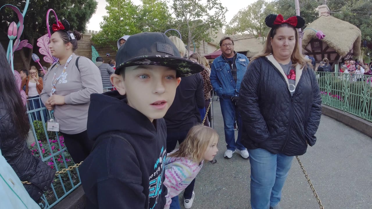 Boy and little girl standing near adults and green railings in a crowded queue.