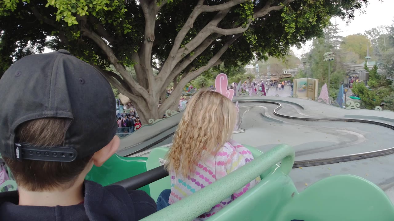 Green ride car approaches a curving section of track with children seated ahead.