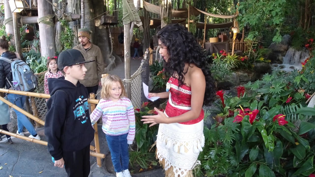 Boy and girl listen as a costumed woman talks beside flowers.