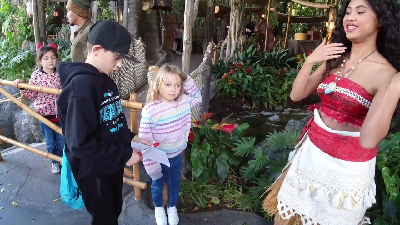 Boy and girl stand near a costumed woman in a planted theme-park area.