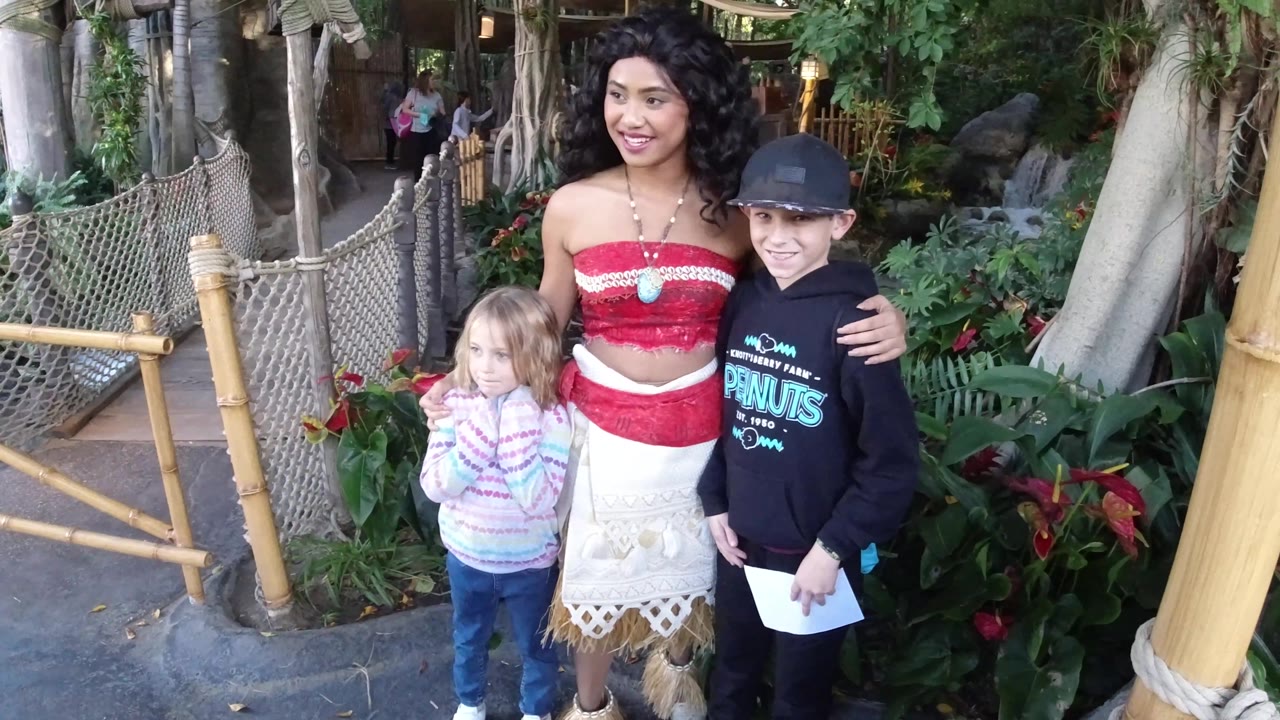 At Disneyland California, the woman and two children face more squarely toward the camera, with dense foliage, tree trunks, and bamboo posts filling the background.