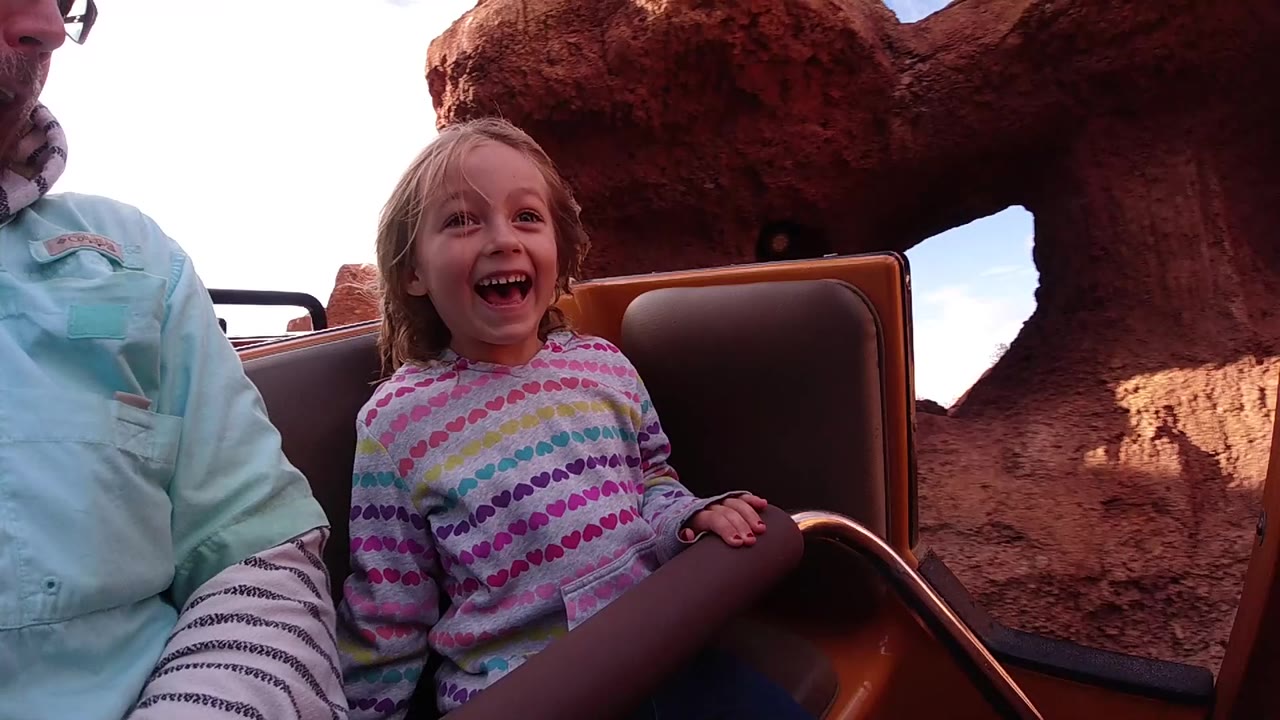 The girl remains centered and smiling in the ride seat at Disneyland California, with a red rock opening and sky visible behind her.