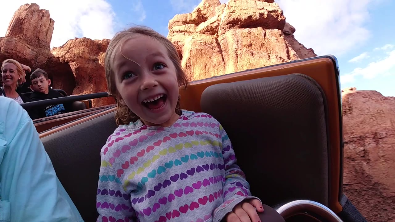 A laughing child fills the foreground of the ride vehicle, with the brown seat back framing the right side and sunlit red rock scenery rising behind at Disneyland California.