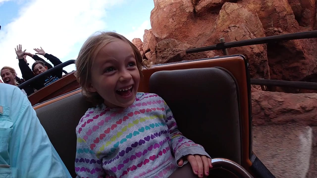At Disneyland California, the child looks upward with an open smile while the ride car passes red rock scenery and other riders remain visible behind her.