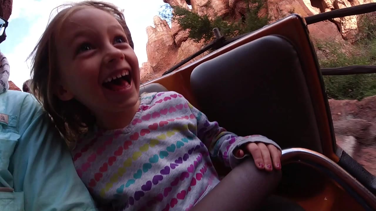 Laughing girl holds the ride seat handle near rock walls.