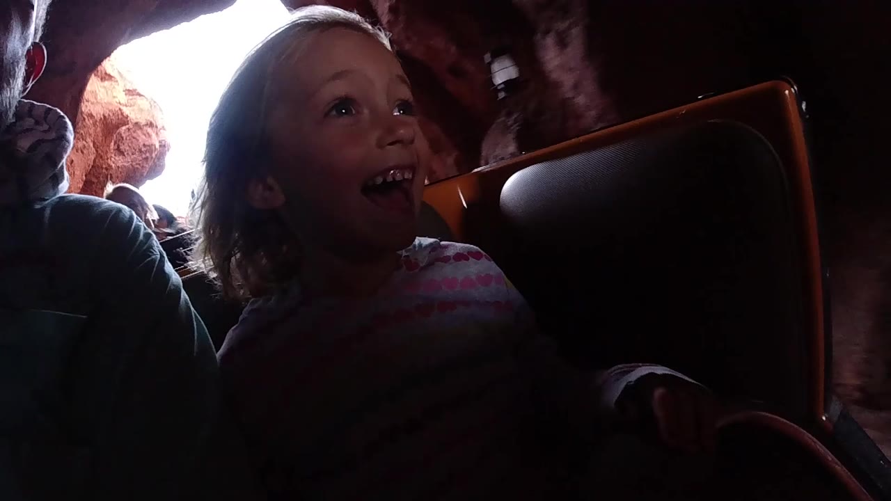 Child grinning beside a coaster seat in a rocky tunnel.