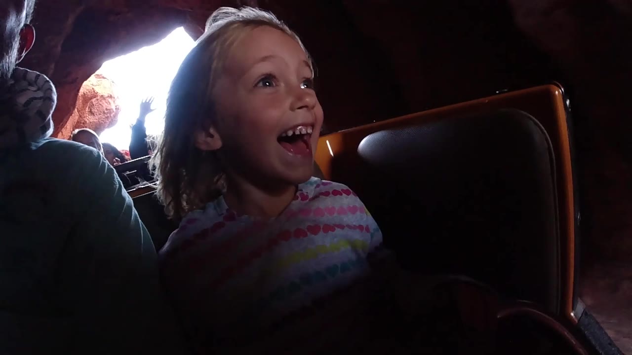 At Disneyland California, the girl laughs with her face turned upward, framed by a dark coaster seat and a bright cave opening behind the car.