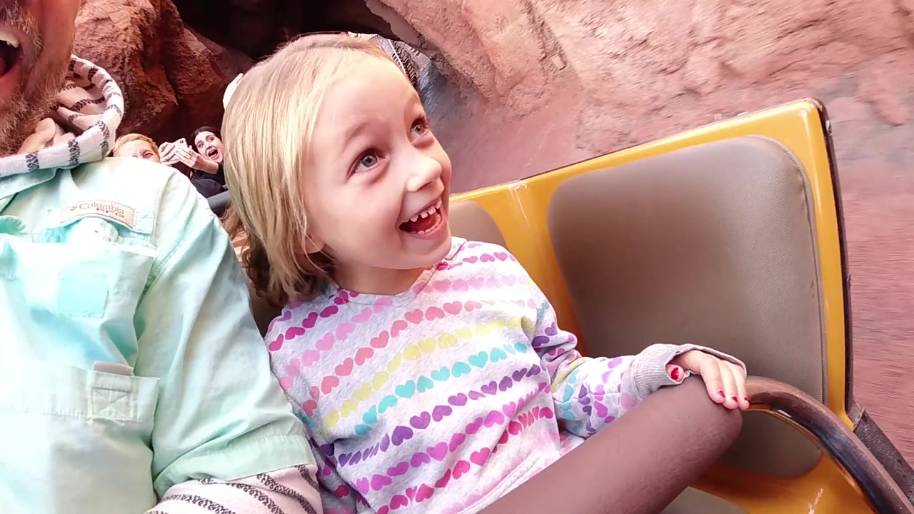 Young girl grinning and looking upward from a ride car.