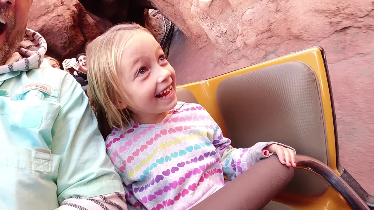 At Disneyland California, the child remains framed close in the ride car, smiling toward the upper right while red rock walls and the yellow seat form the background.