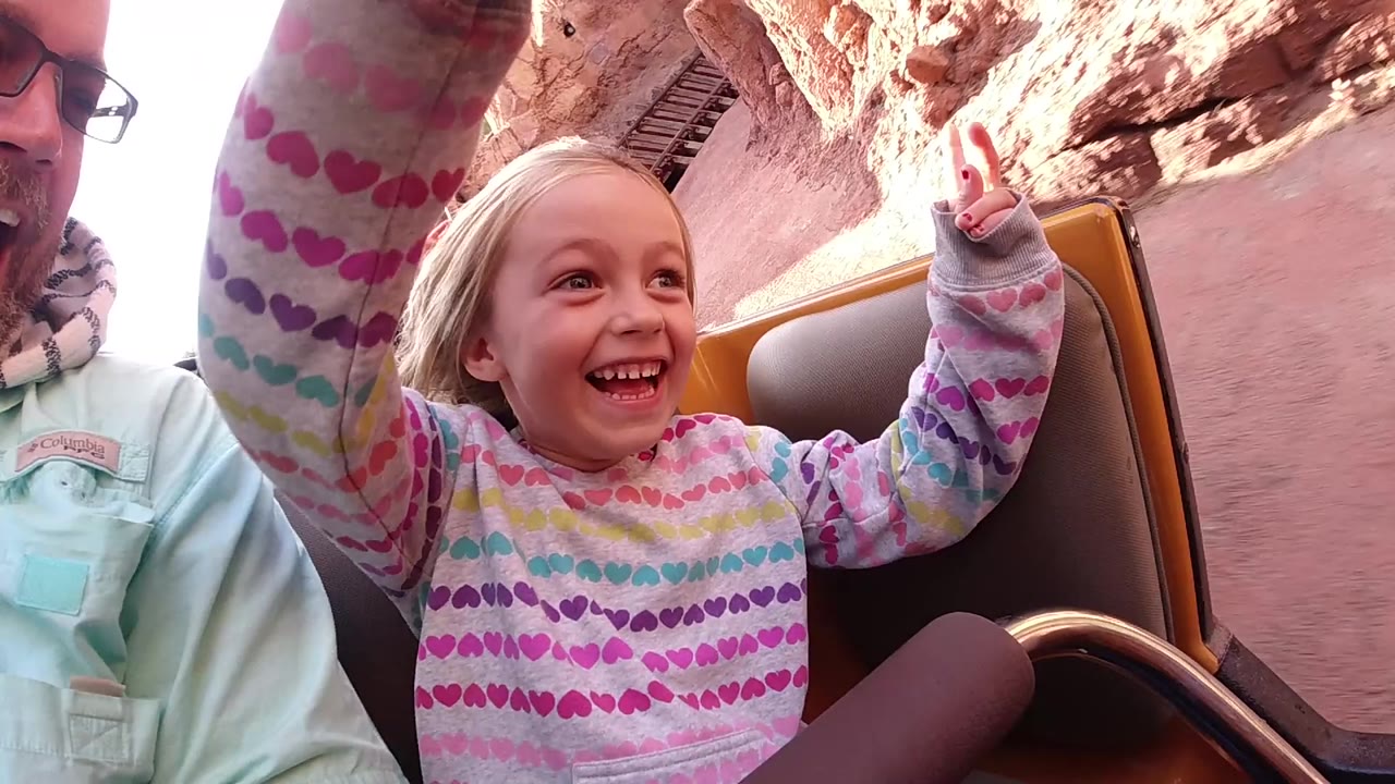 Girl laughing with both hands up while the ride passes reddish rockwork.