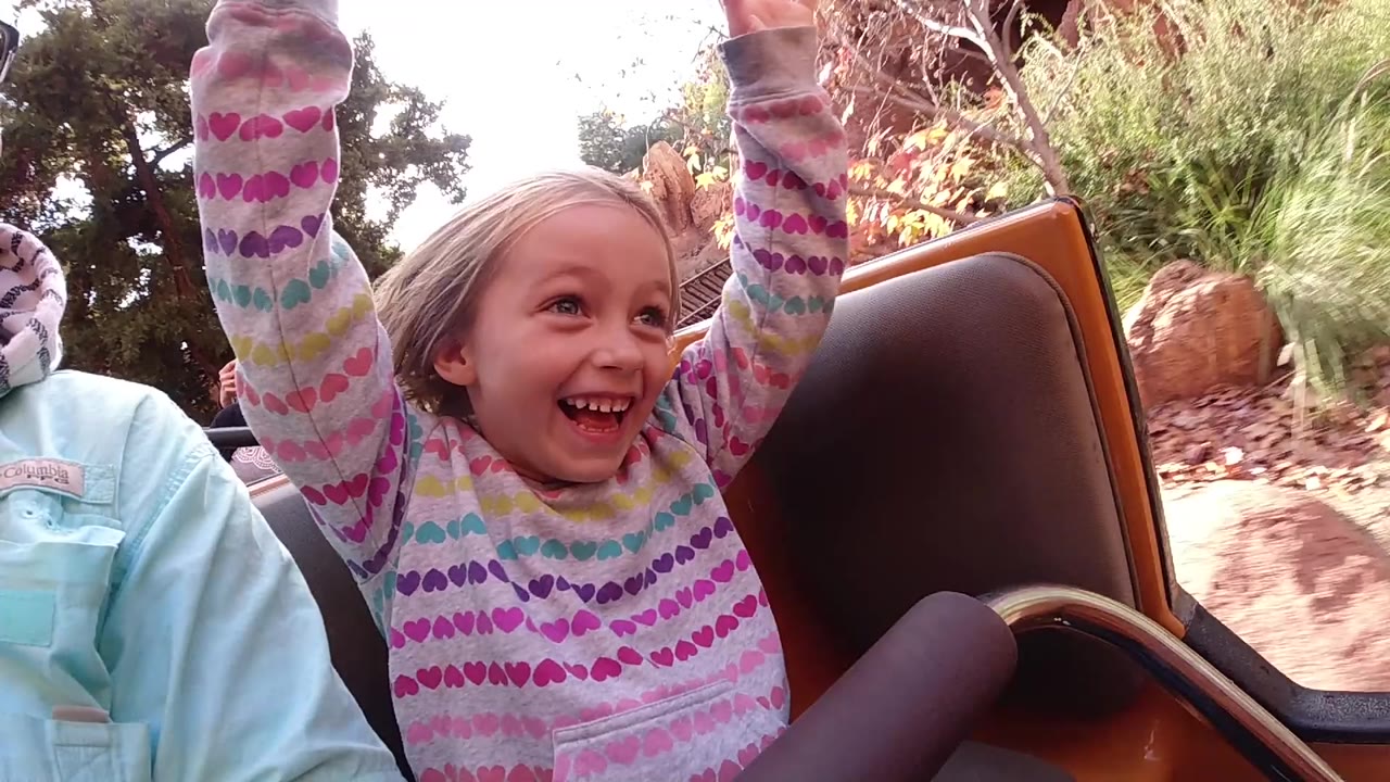 Smiling child in a patterned top riding beside an adult.