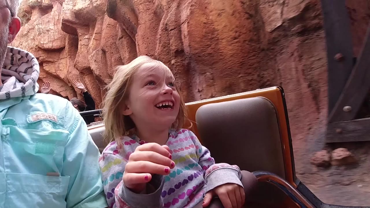 At Disneyland California, the child looks upward and smiles from the roller coaster seat while the adult's shoulder and chin remain cropped at the left side.