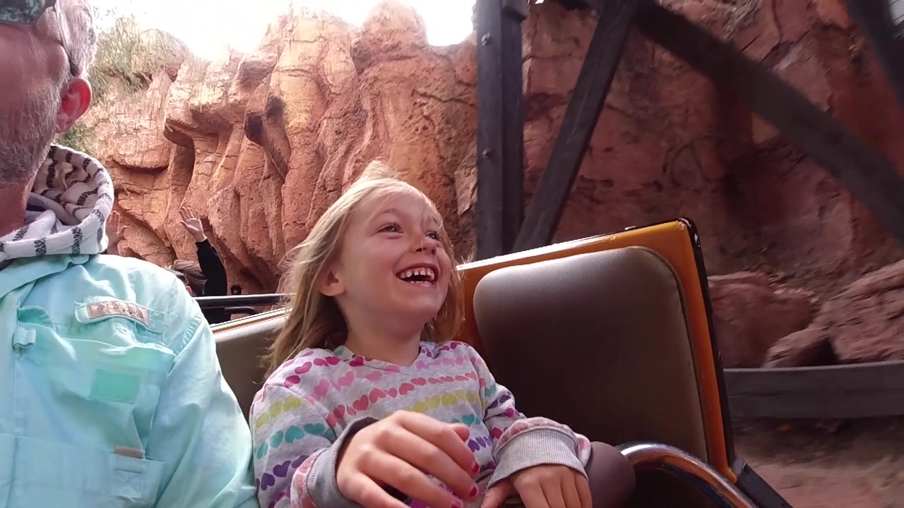 Child and adult riding past red mine-style rock scenery in a coaster car.