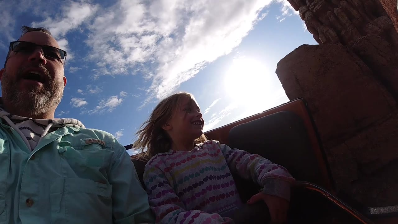 Father and daughter on coaster passing near tall red rock.