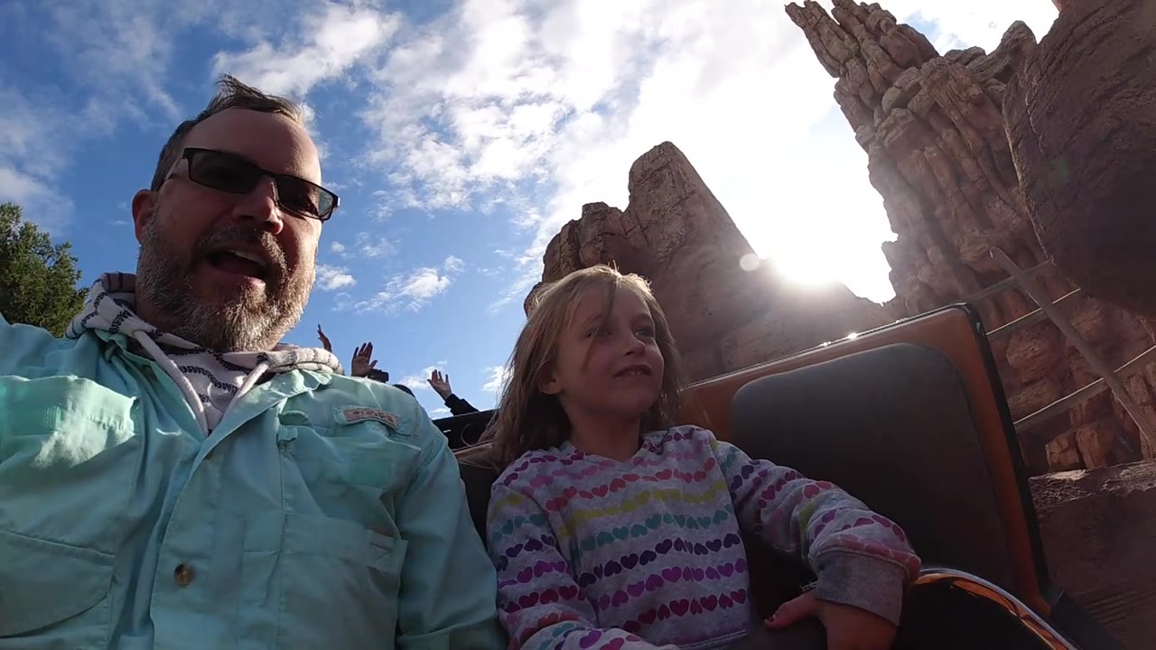 Backlit father and daughter in a roller coaster car passing canyon scenery.