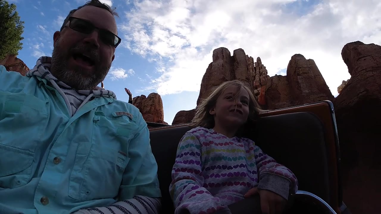 Adult opens his mouth while a child smiles in a roller coaster car.
