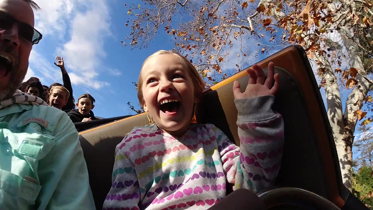 At Disneyland California, the girl grins with her palm raised near the seat back while an adult in sunglasses and riders behind her remain visible.