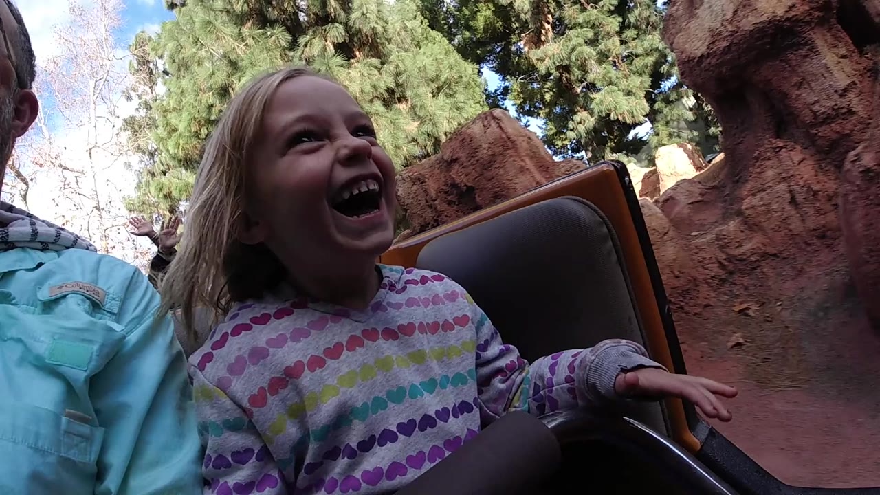 Girl laughs in a ride seat with red rock and trees behind her.