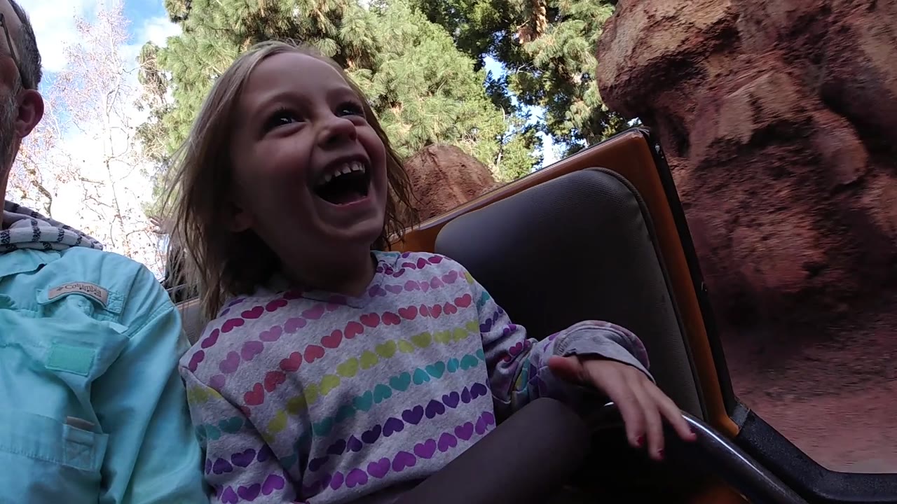 At Disneyland California, the girl laughs with her hand near the ride side panel as a red rock wall fills more of the background behind the seat.