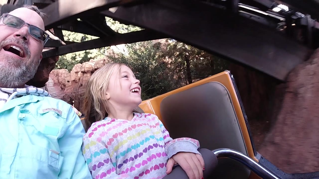 Father and daughter pass under dark ride beams.