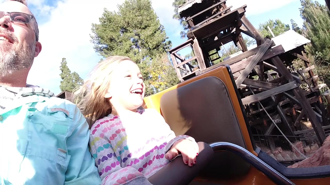 At Disneyland California, the girl laughs with her face turned slightly upward while the adult man remains partly cropped at the edge and the coaster structure passes behind them.