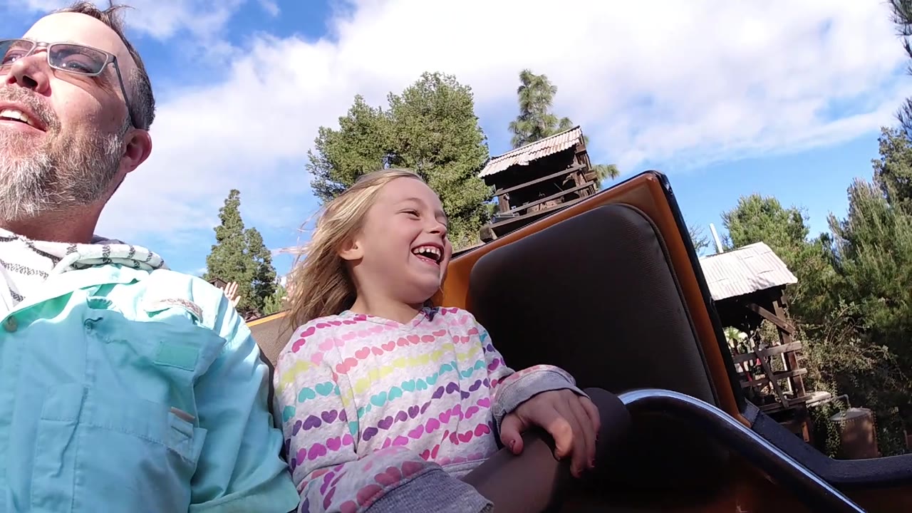 Adult man and girl laughing as the coaster car moves past trees.