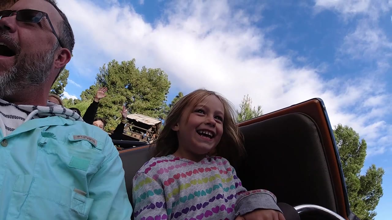 At Disneyland California, the man opens his mouth in a shout while the girl laughs, and a background rider raises a hand above the coaster car.