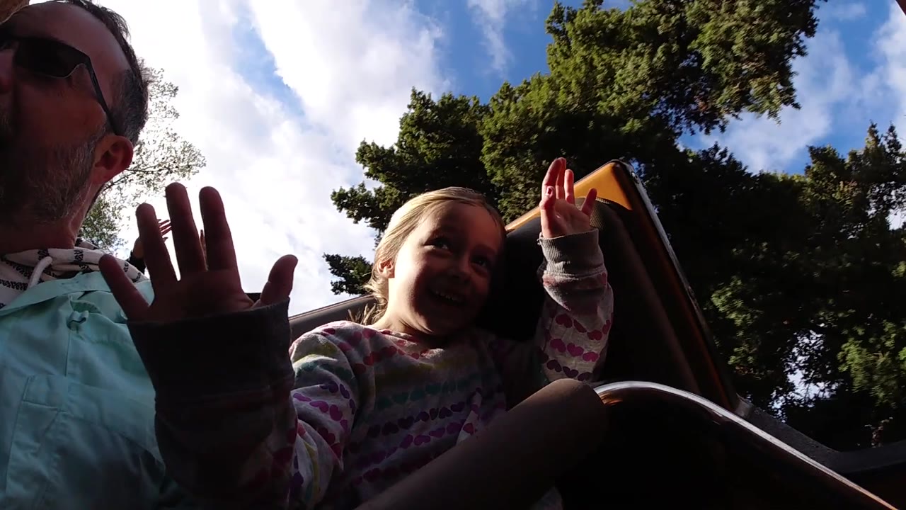 Girl looks up from a ride seat while a man sits beside her.