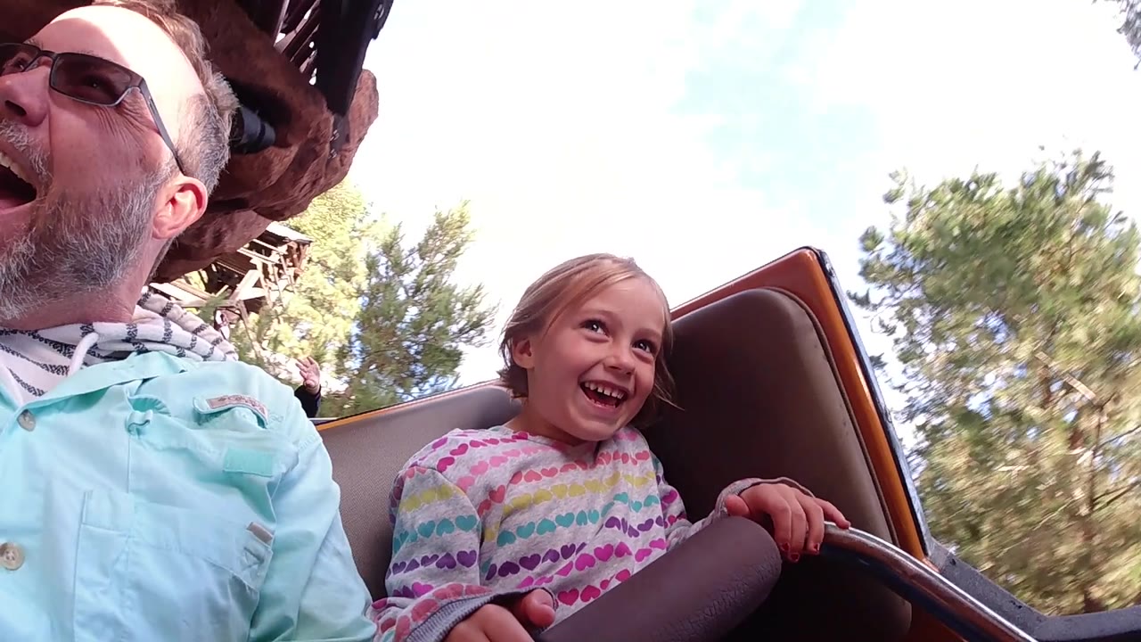 Girl laughing on a ride while her father is partly cropped at left.